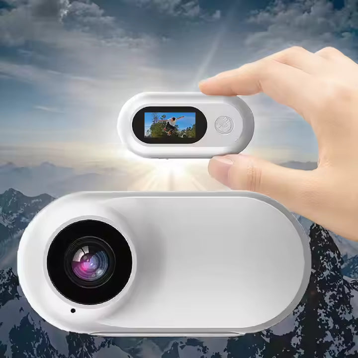 Hand holding the compact Mini-Motion View mini action camera outdoors, showing lens and screen with mountain scenery