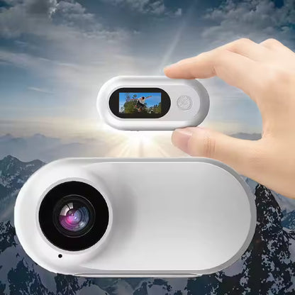 Hand holding the compact Mini-Motion View mini action camera outdoors, showing lens and screen with mountain scenery